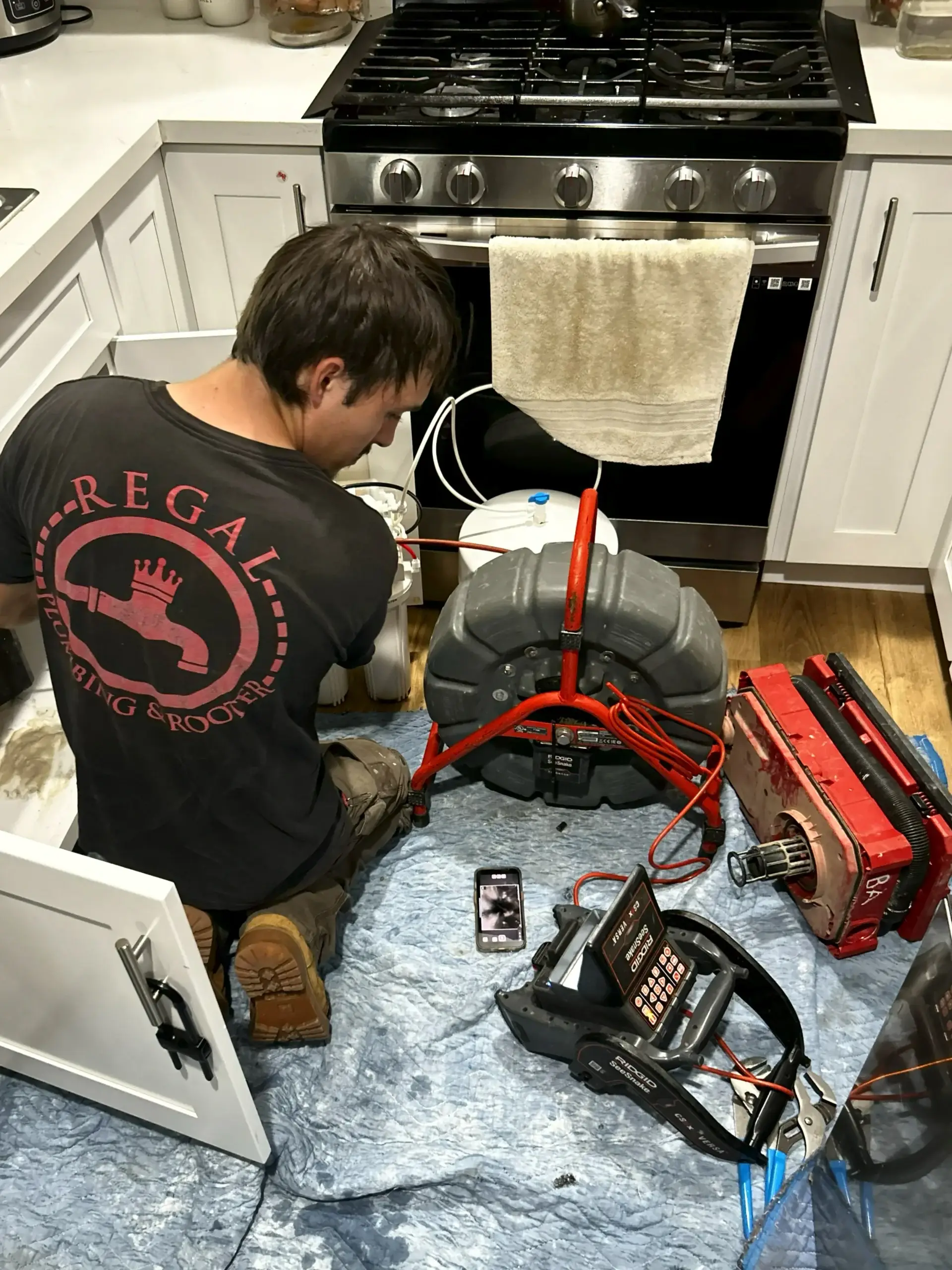 Regal Plumbing & Rooter technician using camera inspection and drain cleaning equipment in a residential kitchen