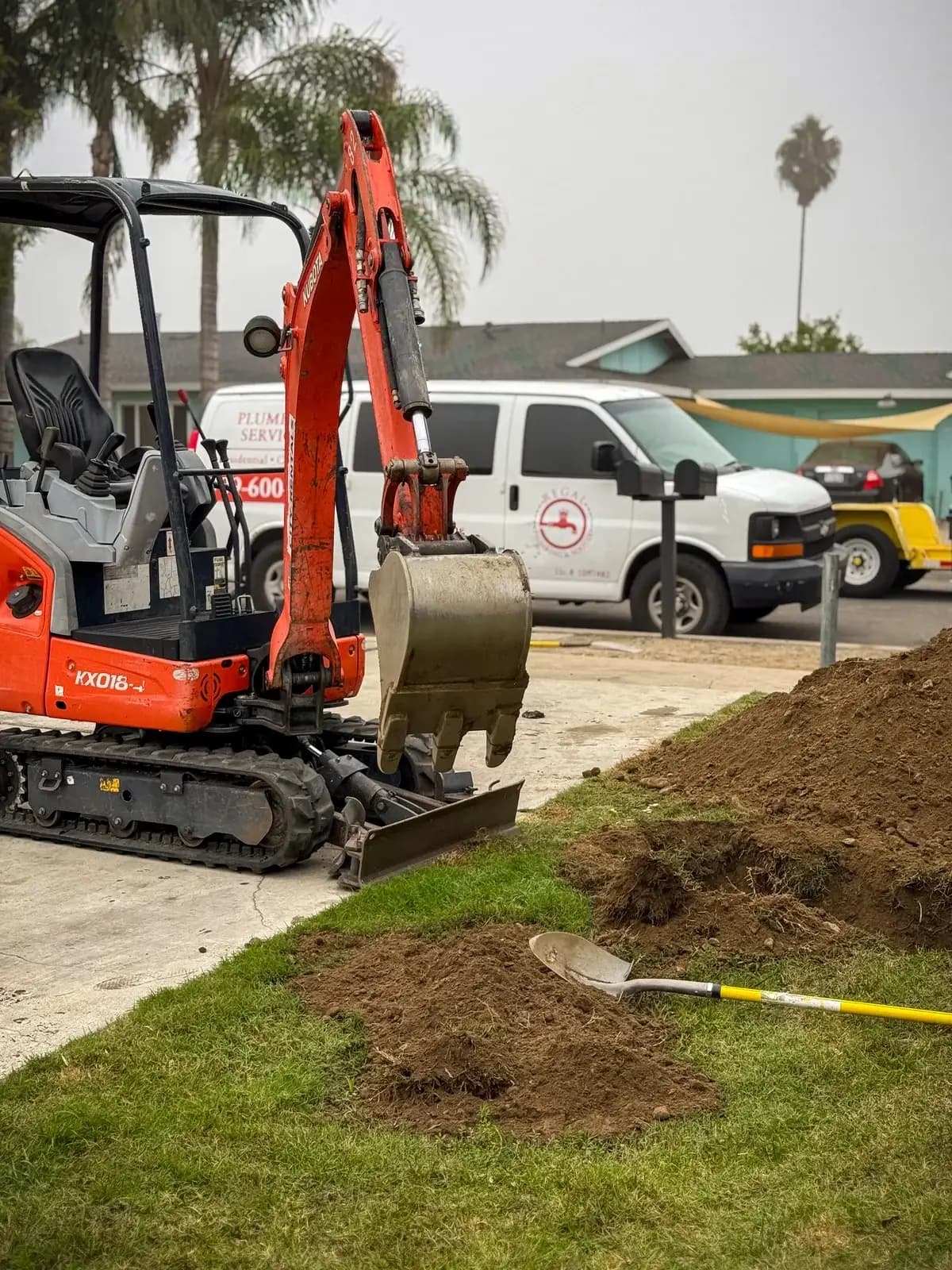 Excavation equipment digging for sewer line repair with Regal Plumbing & Rooter service vehicles in Fontana, CA